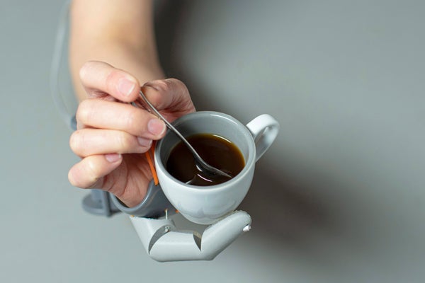 A person supporting a coffee cup with a 3-D-printed appendage while stirring a spoon with their other fingers.