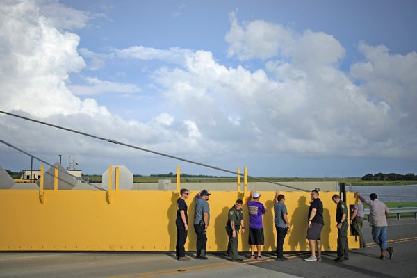Workers stand in front of a bright yellow levee.