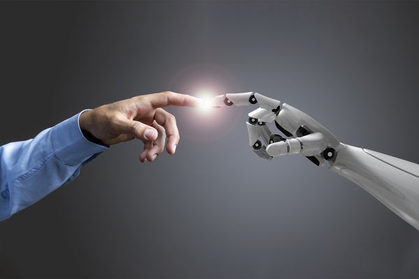 A human arms and hand and robot arm and hand, with index fingers toughing, shown against a grey backdrop.