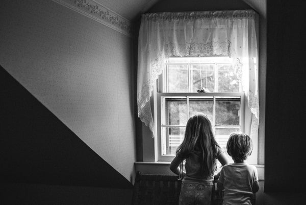 A small boy and girl, seen from behind, gaze out a window.
