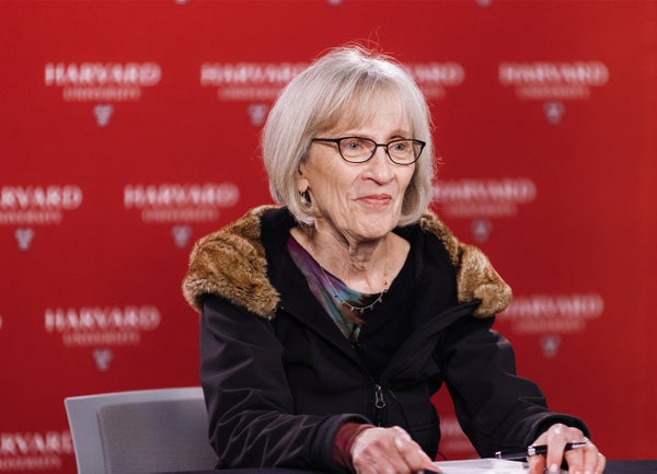 Claudia Goldin seated in front of red Harvard University signage backdrop.