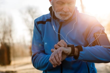 An older man with a beard, wearing athletic clothing, checks a device on his wrist.