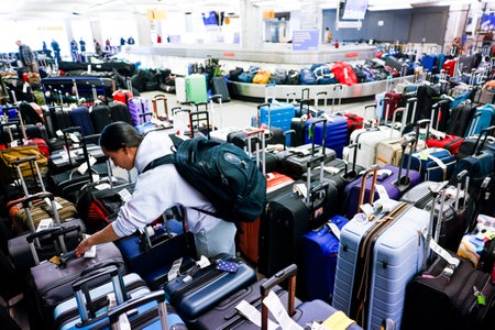 A woman looks at the nametag on a suitcase in the midst of hundreds of suitcases at the airport.