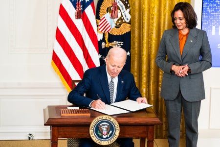 Joe Biden总统坐在办公桌上签署行政命令副总统 Kamala Harris站在左侧
