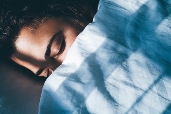 Young woman with curly hair sleeps in bed tossing and turning in dream covered with soft blanket in early morning in bedroom at home