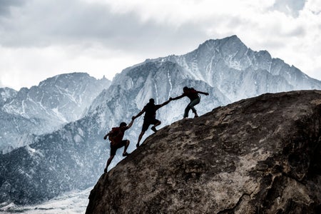 Three friends out rock climbing, helping each other in a dramatic setting