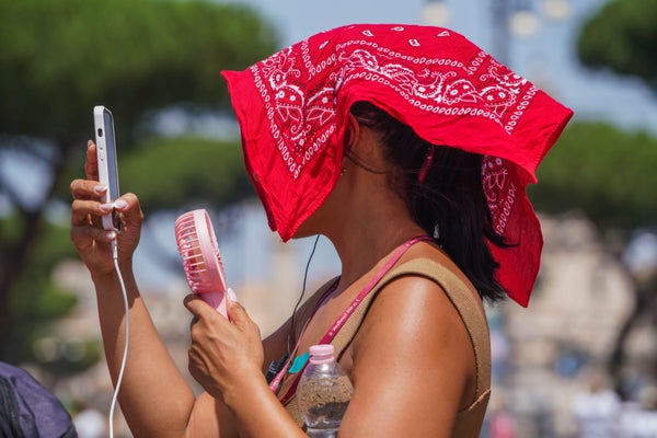Woman with a portable fan covers her head with a bandana