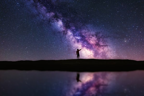 Person pointing up the Milky Way galaxy at night. The scene is reflected in water.