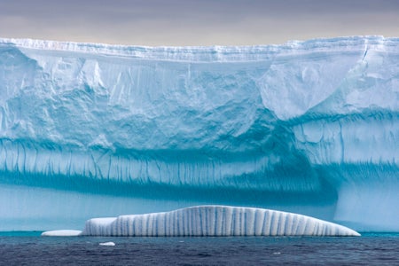 A small iceberg floats in front of a massive glacier.
