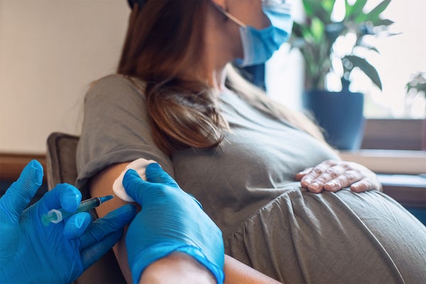 Sitting pregnant person receiving vaccine from medical professional