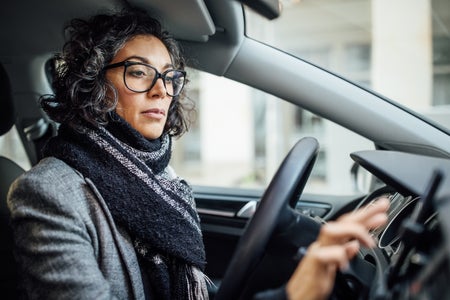 A woman in a car, wearing a scarf and glasses, checks her GPS location.