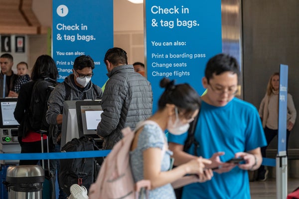 Passengers, some wearing medical face masks, check in at kiosks inside San Francisco International Airport