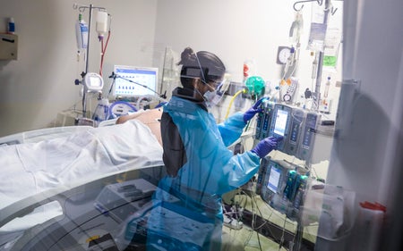 A registered nurse prepares to do a head turn for a patient in a COVID intensive care unit