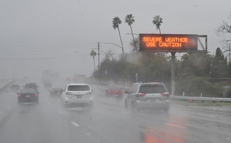 Cars passing by a sign that reads SEVERE WEATHER USE CAUTION during rain on a highway.