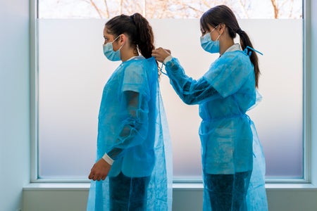 Nurse helping doctor in wearing protective workwear in clinic