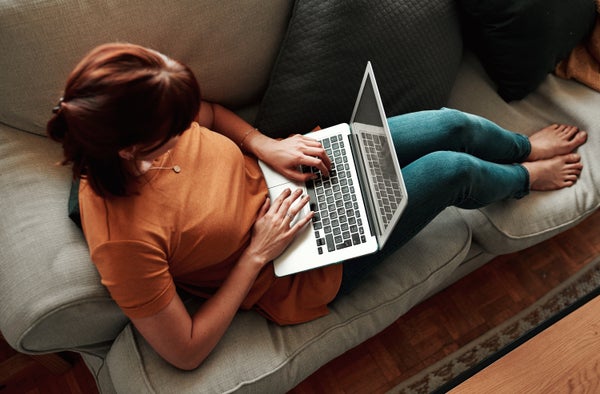 A woman using her laptop while relaxing at home on couch.