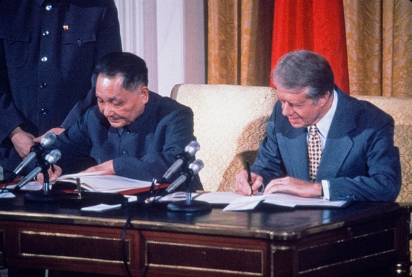 Historical photo of US President Jimmy Carter with Chinese leader Deng Xiao Ping sitting next to each other at a table signing papers