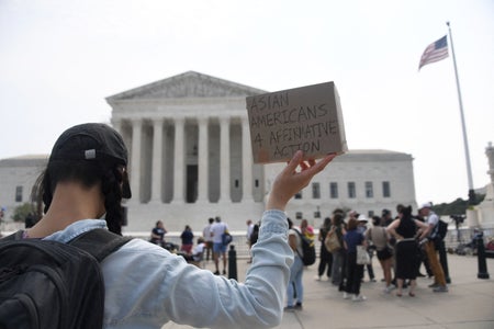 A woman shown behind, holding a sign at an affirmative action protest in front of the Supreme Court.