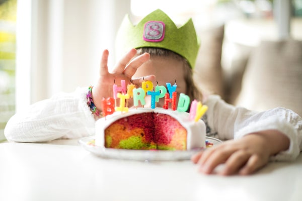 Girl hiding behind festive birthday cake.