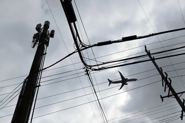 An airplane flies above telephone wires.