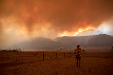 Silhouetted figure stands under bright orange smoke-filled skies