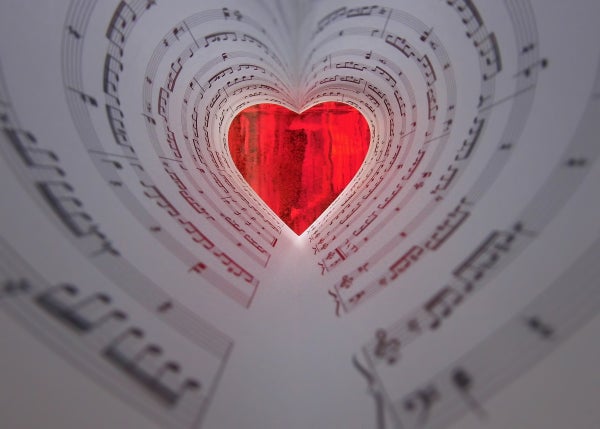 A red valentine at the end of a tunnel made of sheet music.