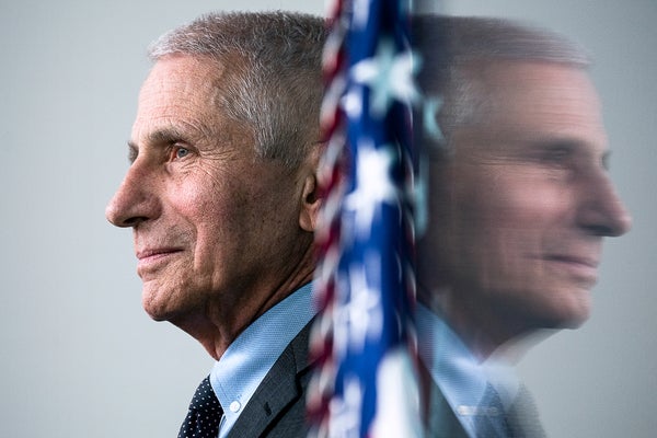 Photograph taken in the White House Briefing Room shows Anthony Fauci in profile at left and his reflection on a television display at right