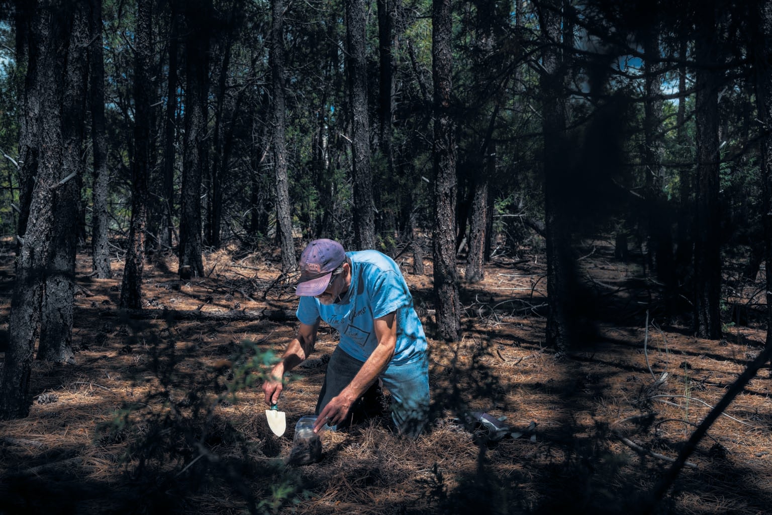 A man kneeling down and scooping dirt into a bag.