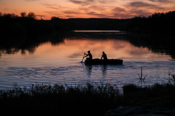 Two men rowing a boat at sunset at the Rio Grande river.
