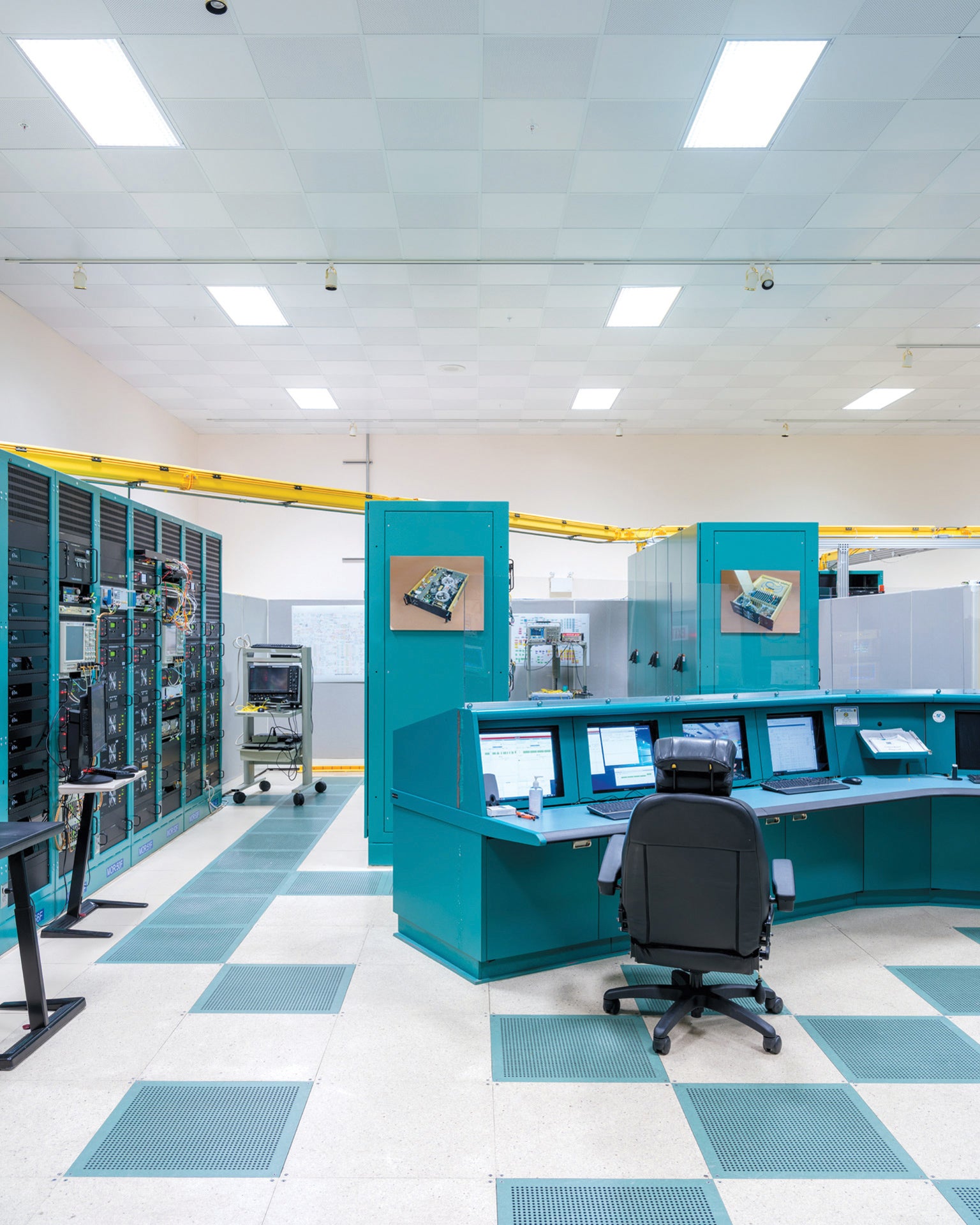   Salle de contrôle avec un bureau bleu et une chaise de bureau, avec des ordinateurs alignés sur un mur.