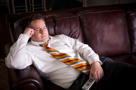 A tired businessman watches television at home after a long day