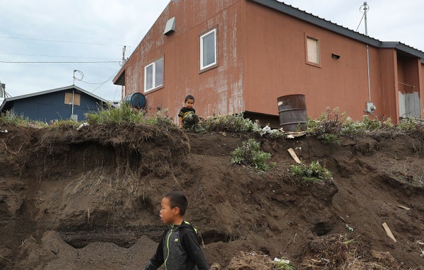 Little boy stands near a home that is dangerously close to a place where the permafrost is melting and being eroded away in Kivalina, Alaska.