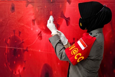 Profile view of police health worker against bright red wall holding COVID vaccine