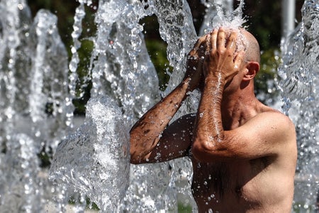 A shirtless man cools off in a public fountain in France.