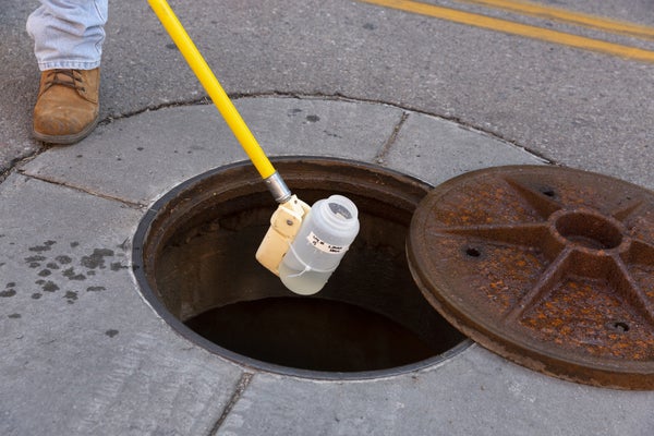 Person lowers bottle into manhole to collect water sample.