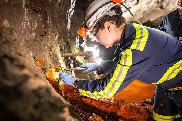 Researcher wearing safety helmet and headlamp collecting a sample in an underground former gold mine