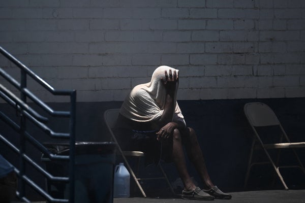 A man in a hoodie sitting outside in the heat covering his face with his hands.