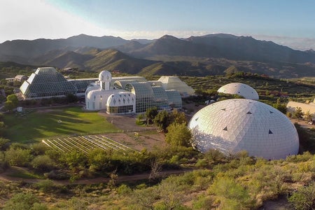 White domes and glass buildings in landscape with mountains in the background.