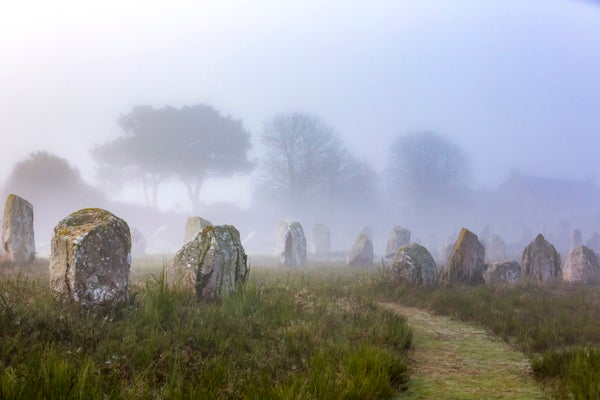 Alignments of menhirs, or standing stones, in the Ménec alignment in France, with misty trees in the background