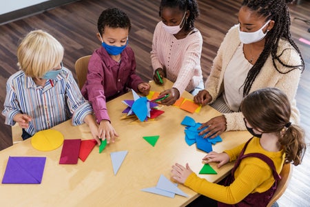 A teacher and four students in a kindergarten or first grade classroom.