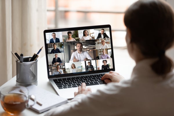 Woman in white shirt on laptop with diverse people collage on computer screen video conferencing.