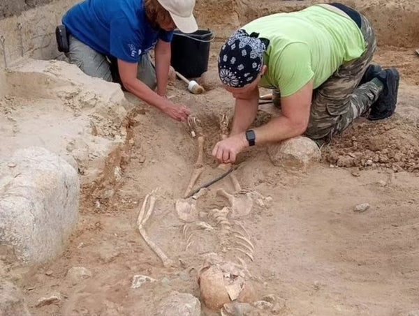 Skeleton of a child buried face-down in the grave surrounded by 2 archaeologists.
