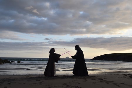Two men in costumes pretend to fight, with the sea in the background.