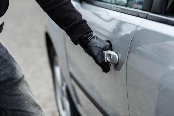 Close up on car thief hand with black gloves pulling the handle of a silver car.