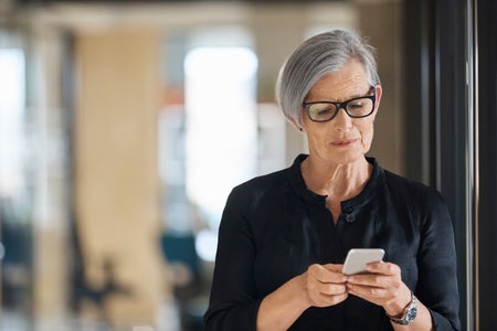 Grey-haired woman types into a smartphone.