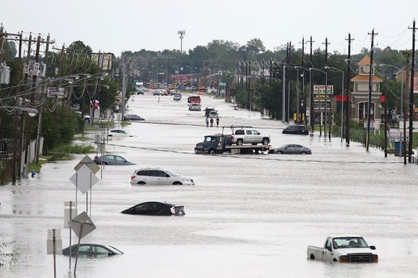 A car gets towed and others submerged in water while men walk in the flooded waters of Hurricane Harvey in Houston.