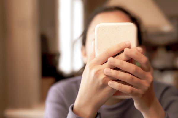 A woman is shown holding a cell phone, which is blocking her face.