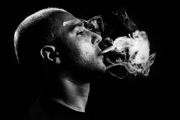 Black and white capture of young man smoking against a black background