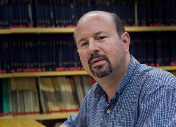 Michael Mann portrait at desk in front on shelving with blue shirt