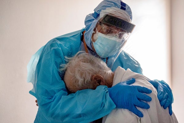 Health care worker wearing PPE hugs elderly patient.